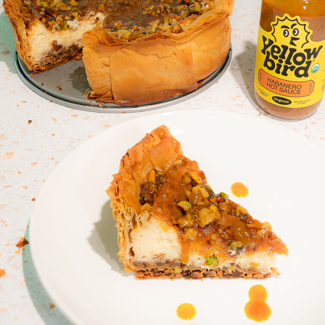 A slice of cheesecake next to a bottle of Yellowbird Organic Habanero Hot Sauce