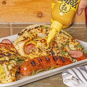 Garlic Shiitake hot sauce being squeezed onto a plate with bratwurst and cooked cabbage. 