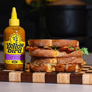 Crispy grilled cheese with caramelized apple, Vidalia onion, sharp white cheddar, prosciutto, and Yellowbird Plum Reaper Hot Sauce on thick-cut artisanal bread.