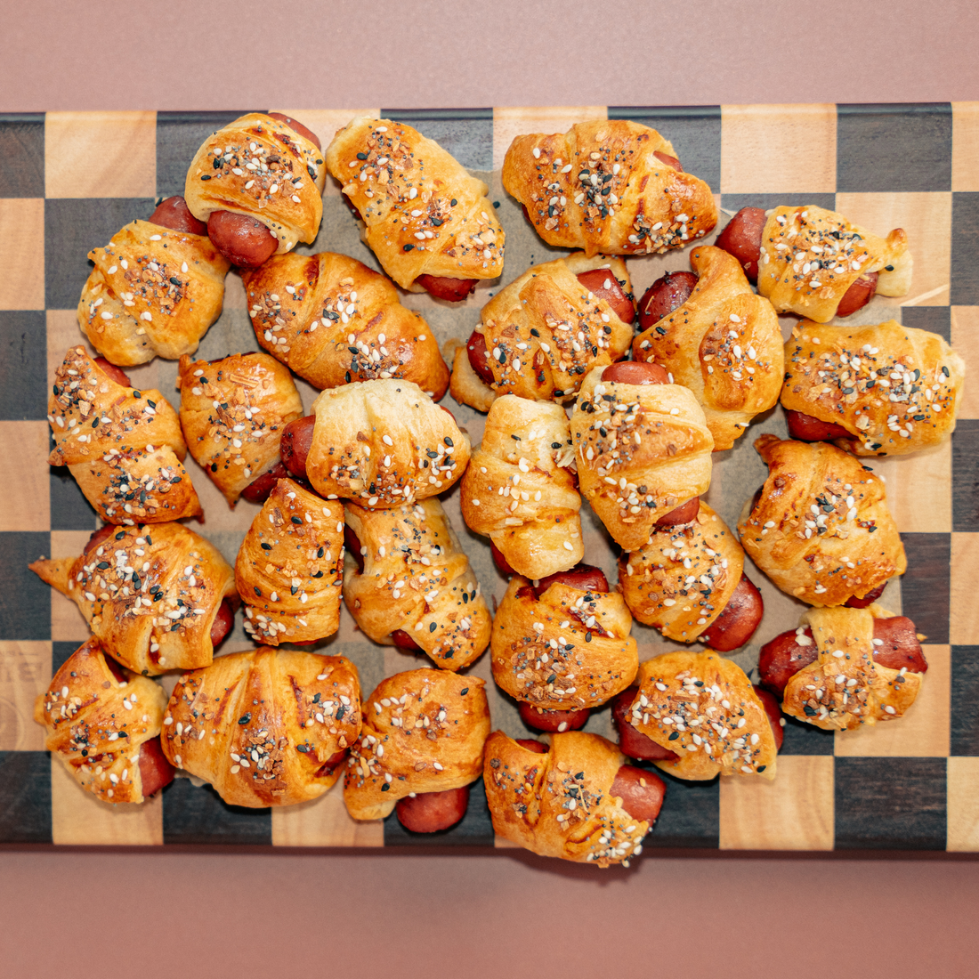 An overhead shot of pigs in a blanket appetizers on a checkered serving board.