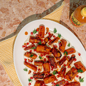 A plate of roasted carrots topped with herbs, pomegranate seeds, and a drizzle of Strawberry Ginger Hot Sauce. 