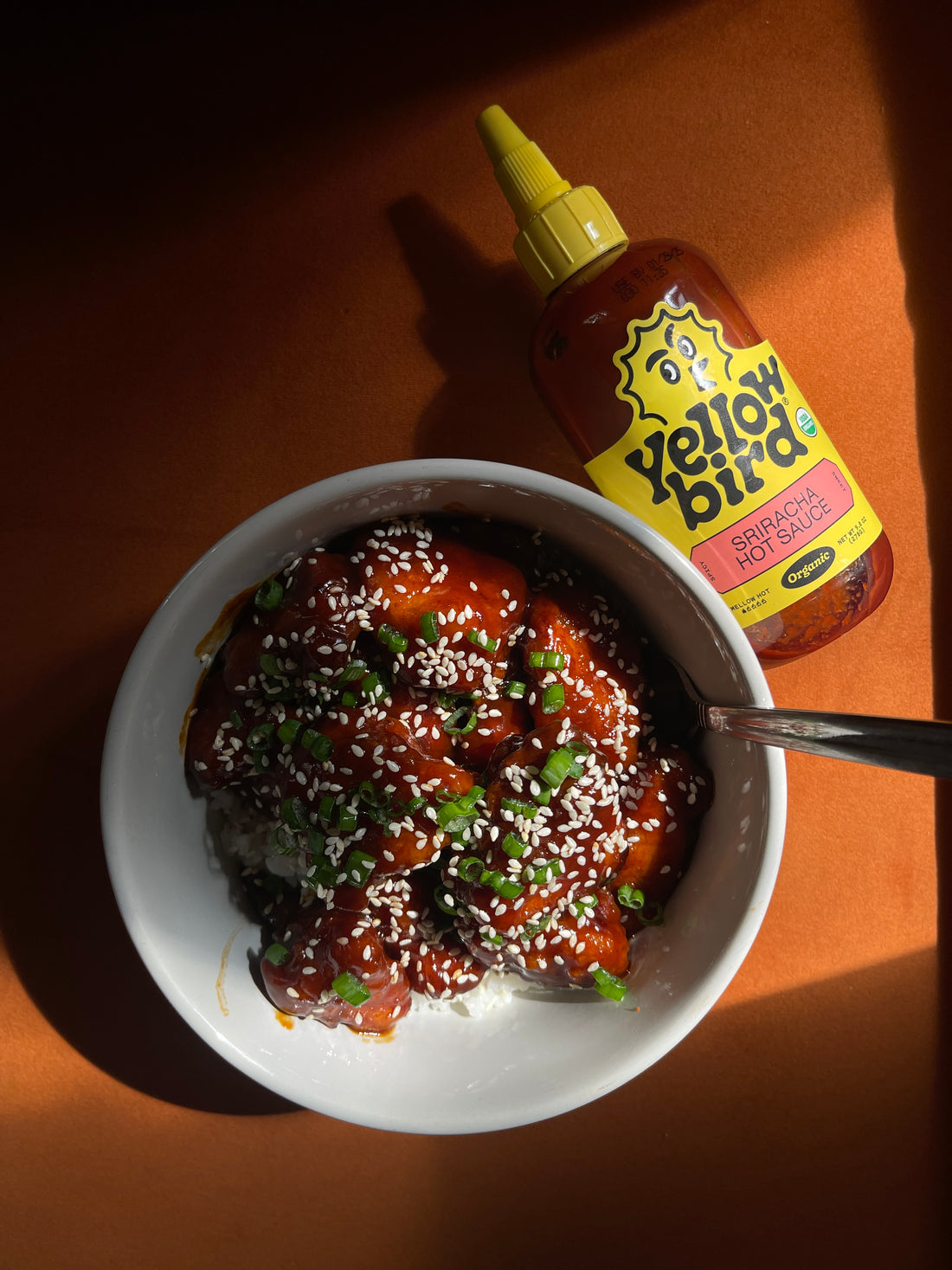 A bowl of Sriracha Firecracker Chicken with a bottle of Yellowbird Sriracha next to it.